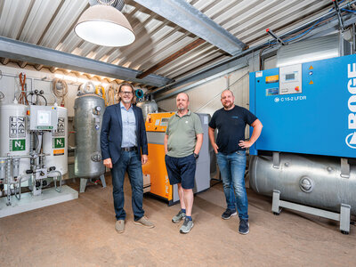 Schraubenkompressor mit drei Männern davor