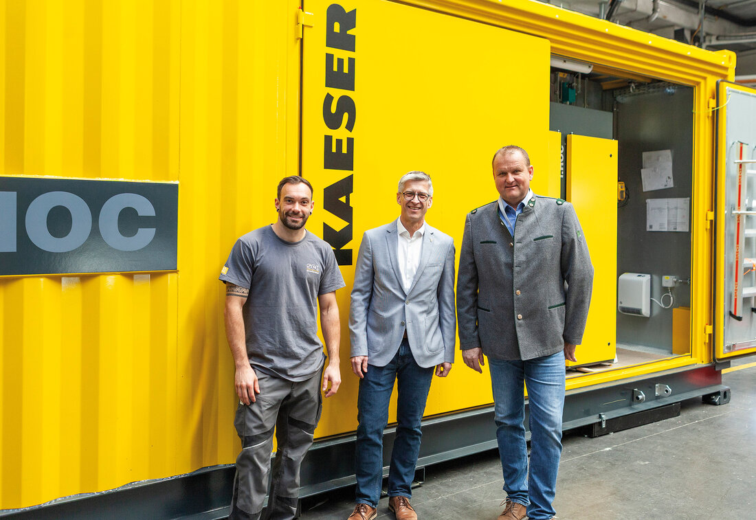 Drei Männer stehen vor einem gelben Kaeser Container