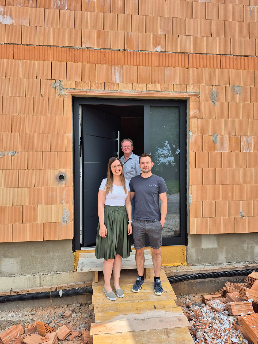 Drei Menschen stehen vor einer Inotherm Haustüre eines Rohbaus